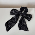 Detail van een zwarte scrunchie met paisley-print en elegante strik van chiffon materiaal - Literair Lint Strik Elastiek - Zwart