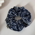Detail eines dunkelblauen Scrunchies mit Blumenmuster und gewebtem Markenetikett - Marineblau Blumen-Saum