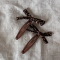 Pair of leopard print bow hair clips on a textured linen fabric background - Leopard Bow Snap Clips Pair