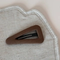 Détail de la pince à cheveux triangulaire en tissu marron sur une surface texturée - Café Triangle