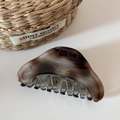 Detail of large acetate hair claw clip featuring dark amber marble pattern and gold text - Tortoiseshell