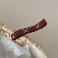 Detailed close-up of red metal hair clip with brown plaid fabric on a woven basket - Red Plaid Wave Straight Clip