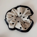 Close-up of beige polka dot scrunchie with black ribbon edges and woven label details - Beige Polka Dot