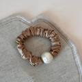 Close-up of champagne satin scrunchie with elegant pearl accent and soft pleats - Apricot