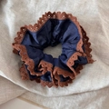 Détail d'un chouchou bleu denim avec bordure en dentelle marron sur fond de lin - Chouchou Anneau de Taille