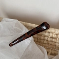 Close-up of tortoise shell pattern acetate hair clip resting on a white woven basket - Dark Leopard Coarse Straight