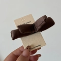 Close-up of brown satin bow hair clip with plush filling on a textured branded card - Brown