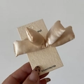 Vista dettagliata del fermaglio per capelli con fiocco di raso champagne su carta - Beige