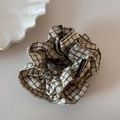Detail van een handgemaakte haarelastiek met zwart-wit ruitpatroon en geweven label - Beige