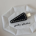 Close-up of a triangular black hair clip with white stitching details on a quilted mat - Black Yellow Edge