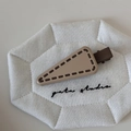 Detailed macro view of cream-colored triangle hair clip with decorative stitching textures - Dark Coffee Edge