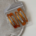 Detalle de cuatro pinzas BB naranja ámbar con textura de mármol en bolsa transparente - Café Vintage