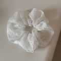 Detailed close-up of white lace scrunchie fabric with fine mesh texture and woven label - White