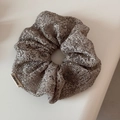 Close-up of silver mesh scrunchie with metallic texture and branded fabric label - Gray