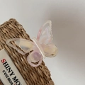 Detail view of a colorful iridescent acetate butterfly hair clip on a woven basket - Translucent White Pink