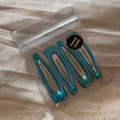 Detail of 4-piece set of teal blue resin hair clips in clear packaging on linen cloth - Light Blue