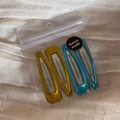 Detail view of 4-piece set of matte mustard and teal snap hair clips in clear packaging - Light Blue & Yellow