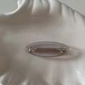 Detail of grey oval hair clip featuring rhinestone flower accents on a shell plate - Clear