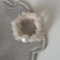 Close-up of off-white mesh hair scrunchie with delicate pleats and a large pearl bead - Beige