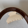 Detail der eleganten cremefarbenen Haarklammer mit glänzender Oberfläche auf Stoff - Cremeweiß