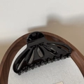 Detail view of a glossy black fan-shaped hollow hair claw clip on a rustic wooden tray - Black