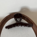 Close-up of a glossy deep red hair claw clip on a circular wooden tray with shadows - Glossy Brown