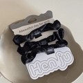 Detailansicht von drei schwarzen Satin-Haargummis auf einer eleganten weißen Displaykarte - Schwarze Kombination