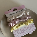 Detaillierte Ansicht von drei Satin-Haargummis in Creme, Rosa und Gelb auf einem Keramikteller - Beige-Rosa-Gelbe Kombination