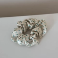 Detailed close-up of cream satin scrunchie with blue polka dots and silver metal logo tag - Small Polka Dot Green