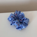 Close-up of light blue satin scrunchie with red heart patterns and silver brand tag - Small Heart Deep Blue
