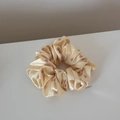 Close-up of beige satin scrunchie with purple heart patterns and a silver brand charm - Small Heart Yellow