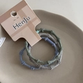 Detalle de tres gomas de pelo trenzadas en colores Morandi sobre un plato de cerámica - Verde azulado