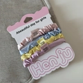 Detail of four colorful satin elastic hair scrunchies on a branded card display - Pale Blue