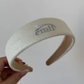 Gros plan sur un serre-tête en similicuir crème avec logo brodé argenté et doublure douce - Serre-tête / Jaune