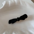 Close-up of a glossy black acetate double-layered bow hair clip on a white ceramic plate - Black