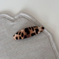 Detail showing the oval leopard print hair clip with fabric texture on a beige mat - Beige Coffee Leopard - Oval Clip