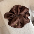 Détail d'un chouchou en satin marron avec une plaque logo ovale dorée élégante - Marron