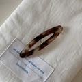 Close-up of tortoise shell pattern acetate hair clip on a white textured background - Tortoise