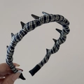 Detail of plaid fabric headband with black punk spikes held against grey wall - Navy White Plaid Long Tooth Hairband