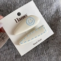 Detail of two-piece cream hair clips with blue smiley face and stitching on display card - White