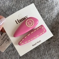 Detail of pink geometric hair clips with yellow smile face on a display card - Pink