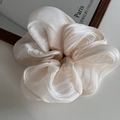 Detailed close-up of cream-colored pleated satin scrunchie with subtle pearl luster - Beige
