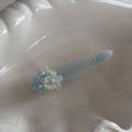 Close-up of a light blue floral hair clip with small pearls in a white shell dish - Blue