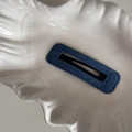 Detail shot of blue denim fabric BB hair clip with fine stitching on a ceramic plate - Dark Blue Denim-Rectangle