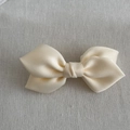 Detailed macro view of a creamy ivory satin ribbon hair bow with smooth silky texture - White
