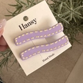 Dettaglio mollette per capelli lilla a onde con cuciture gialle su supporto in carta - Viola