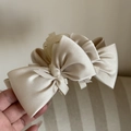 Detailed macro view of large champagne satin bow hair claw clip with silk texture - Beige