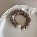 Detail view of smooth champagne satin hair scrunchie featuring an elegant large white pearl - Apricot