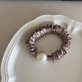 Detalle de un coletero de seda champán con perla grande sobre un plato de cerámica blanca - Caqui