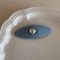 Gros plan sur une pince à cheveux ovale en denim avec cœur argenté sur une assiette - Denim clair